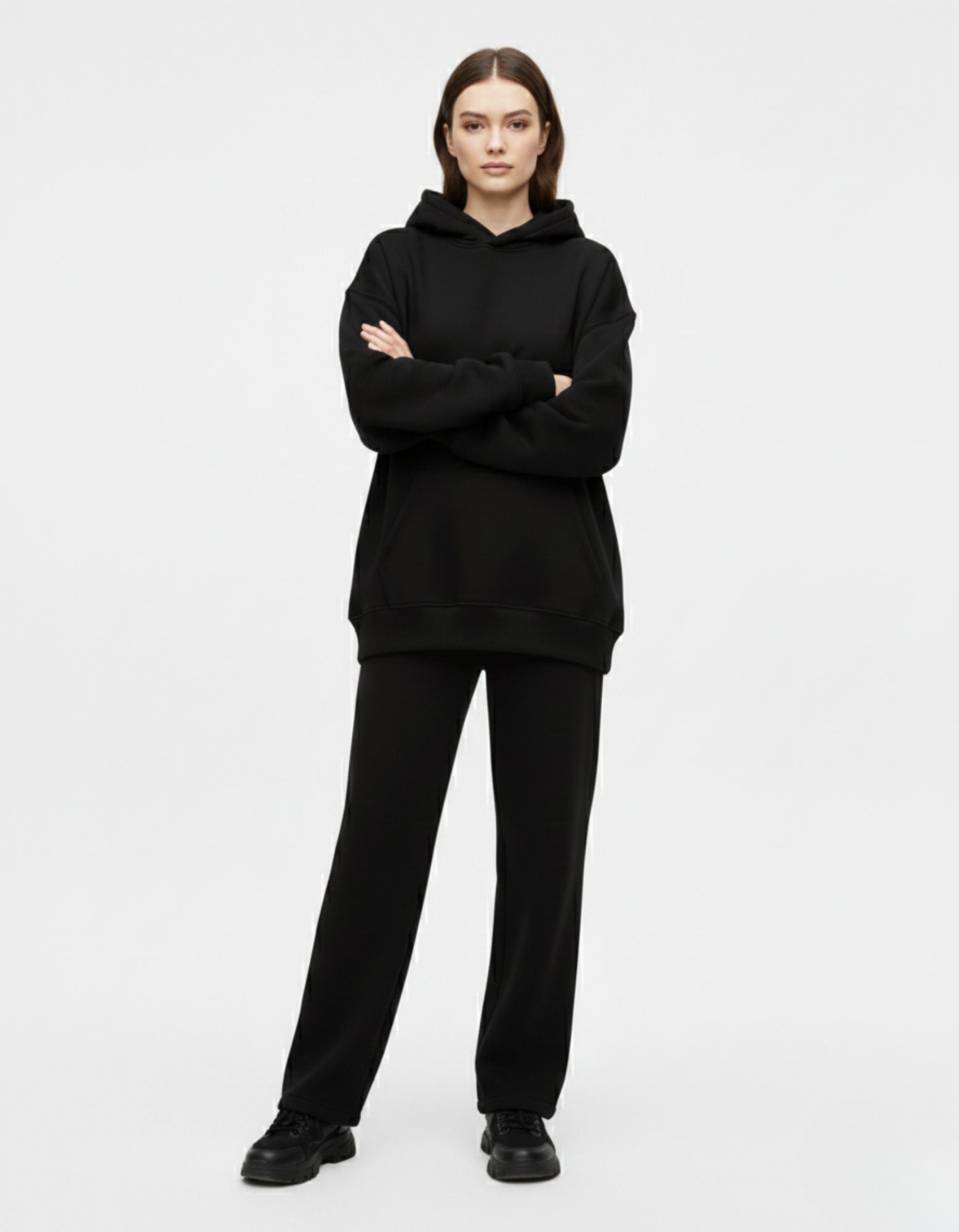 A female model with arms crossed wearing a plain front black minimalist streetwear hoodie with a baggy, comfortable fit.