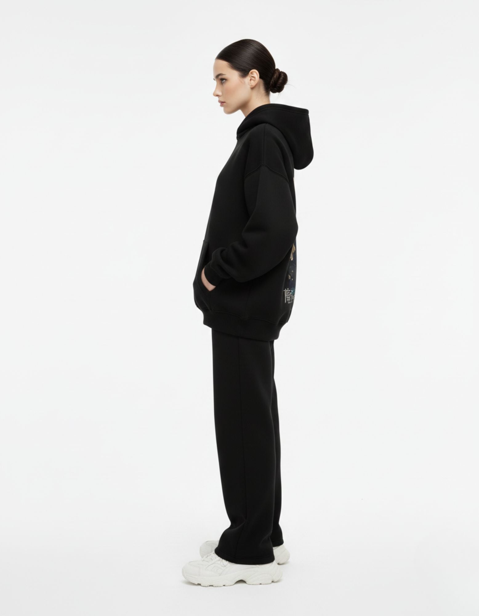 Side profile of a female model wearing an oversized black streetwear hoodie and matching black joggers.