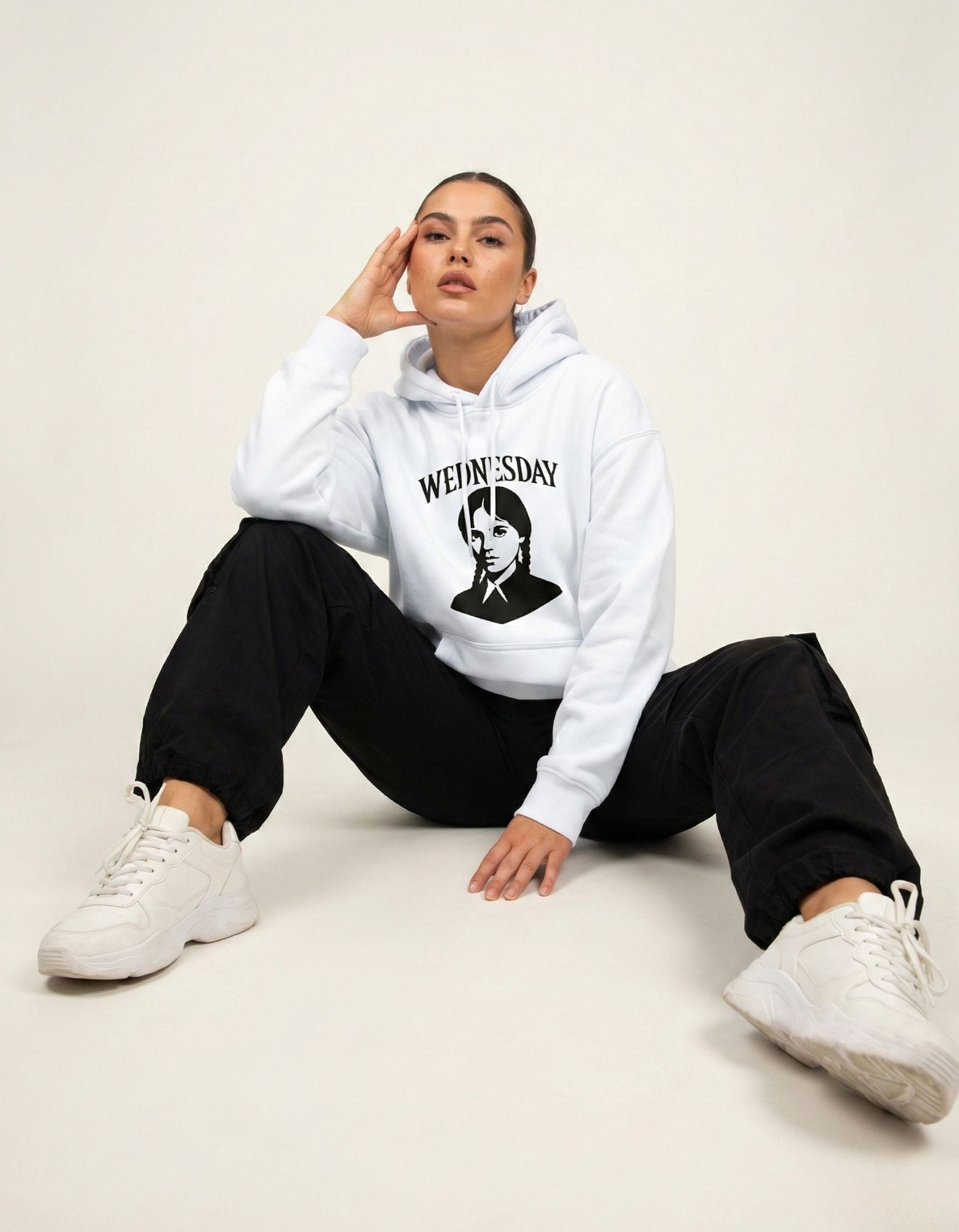 Female model sitting on the floor wearing an oversized light blue Wednesday Addams hoodie, styled for a Gen Z streetwear look.
