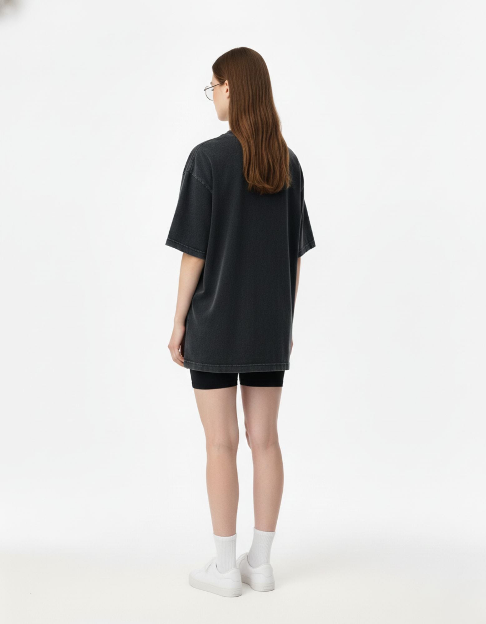 Back view of a female model wearing a loose-fit charcoal acid-wash t-shirt for a minimalist streetwear vibe.
