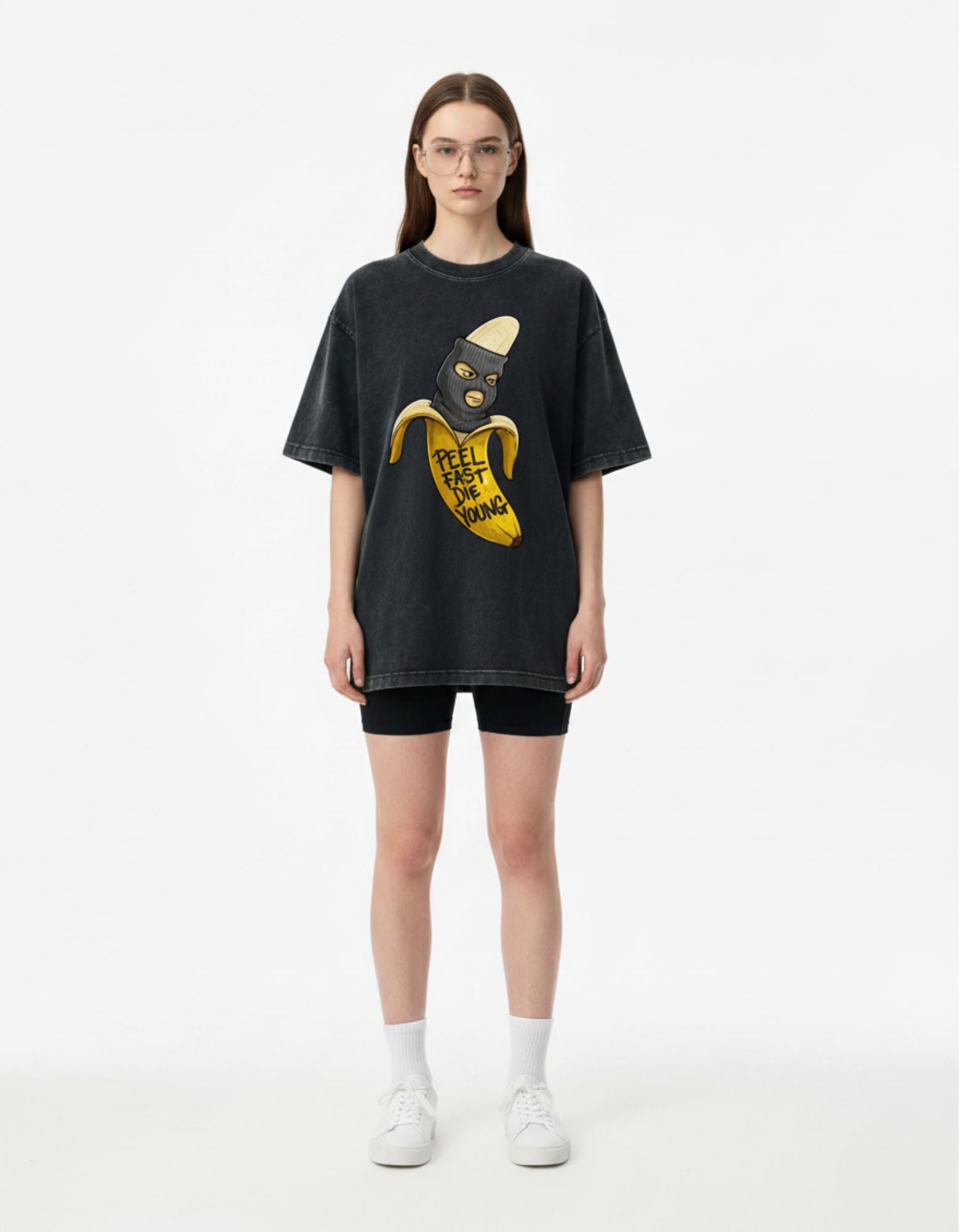 Woman styling a charcoal oversized 'Peel Fast Die Young' banana graphic tee with black biker shorts for an urban look.
