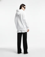 Rear view of a female model in an oversized white "Spider-Verse" graphic hoodie, styled with black wide-leg trousers.