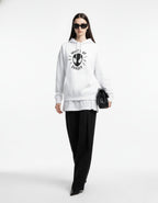 Female model standing in a white Spider-Man graphic hoodie with a black handbag, capturing a trendy Gen Z urban aesthetic.