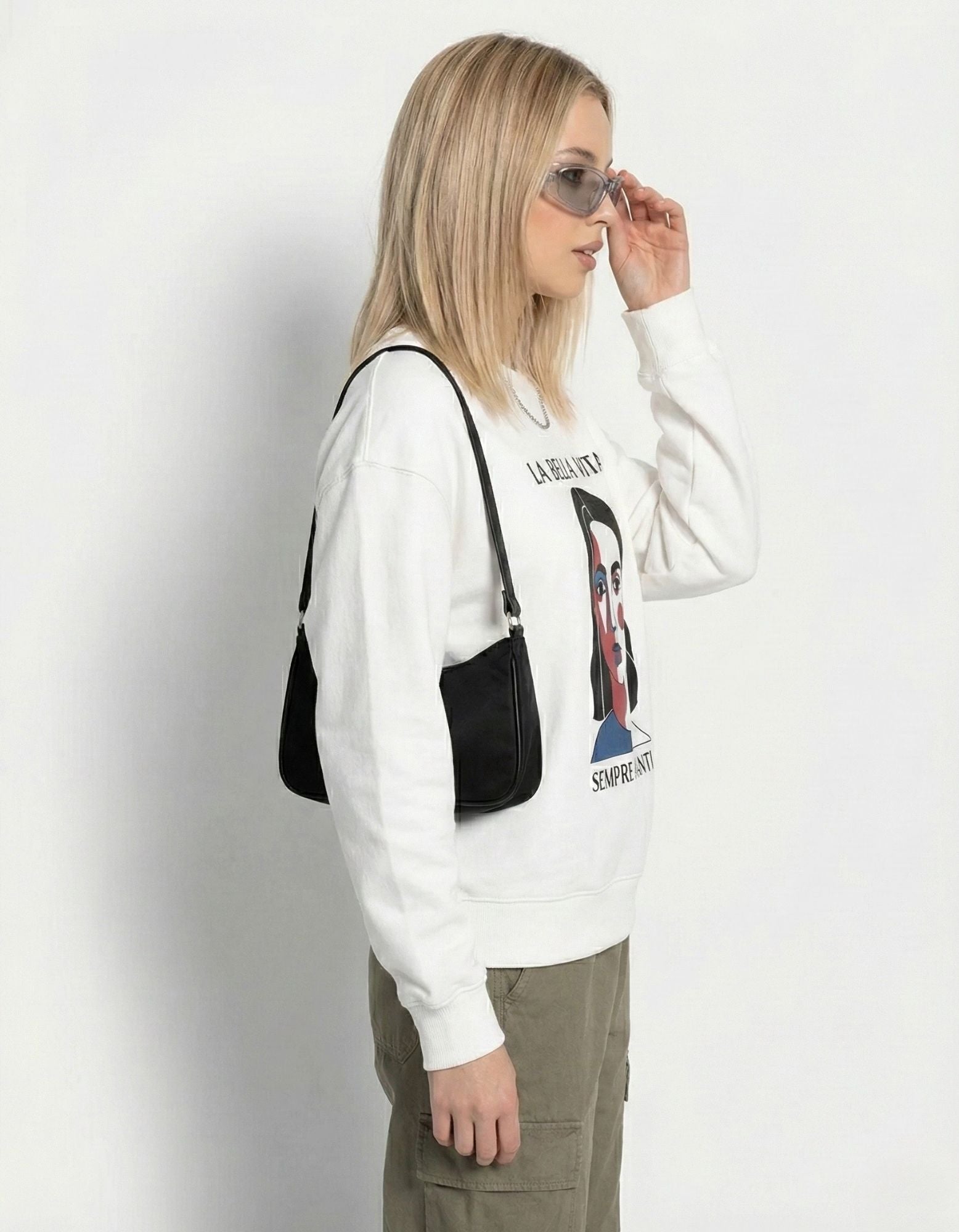 Side profile of a model wearing an oversized white art-inspired sweatshirt with olive cargo pants and a black shoulder bag.