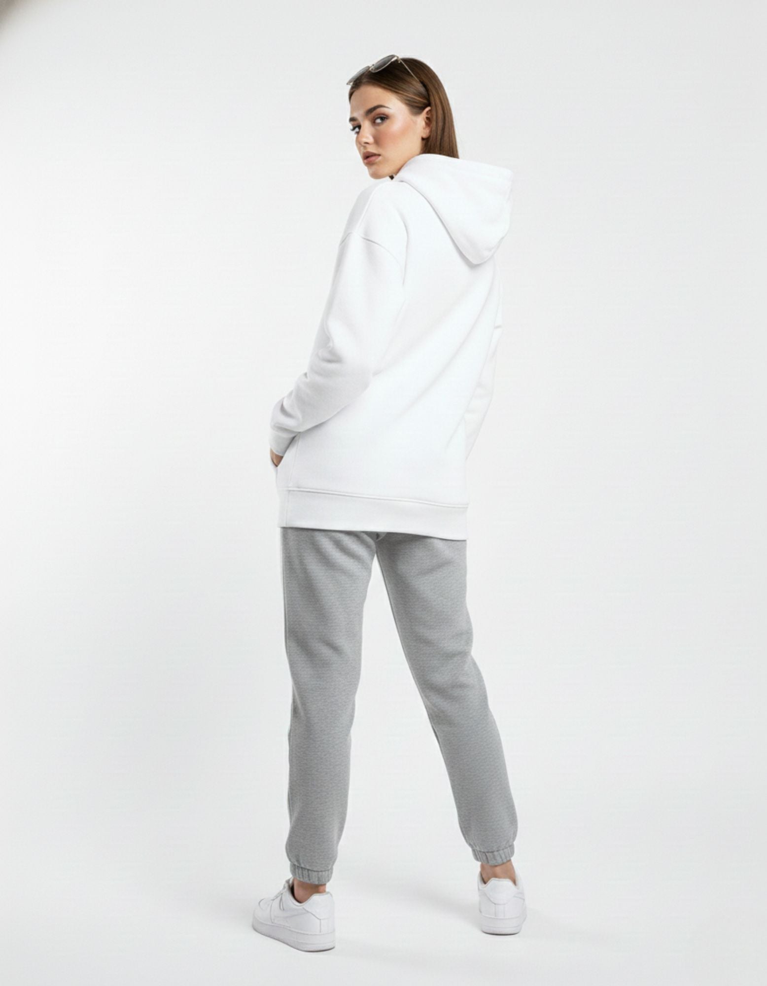 Back view of a white graphic hoodie for women, showing the clean oversized hood and relaxed fit paired with gray sweatpants.