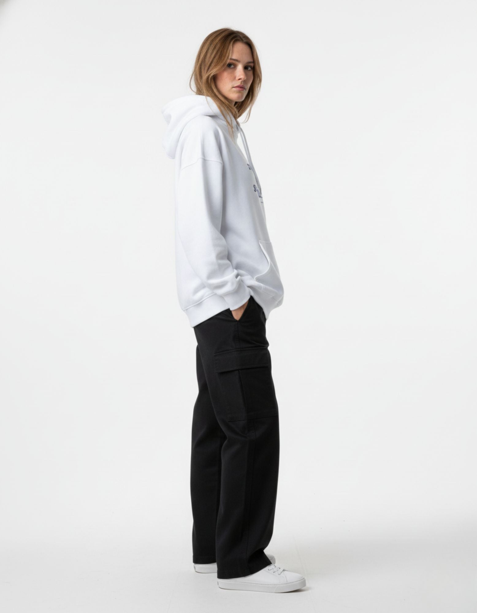 A female model in a white graphic hoodie and black cargo pants, showing the side view of the streetwear-style outfit.